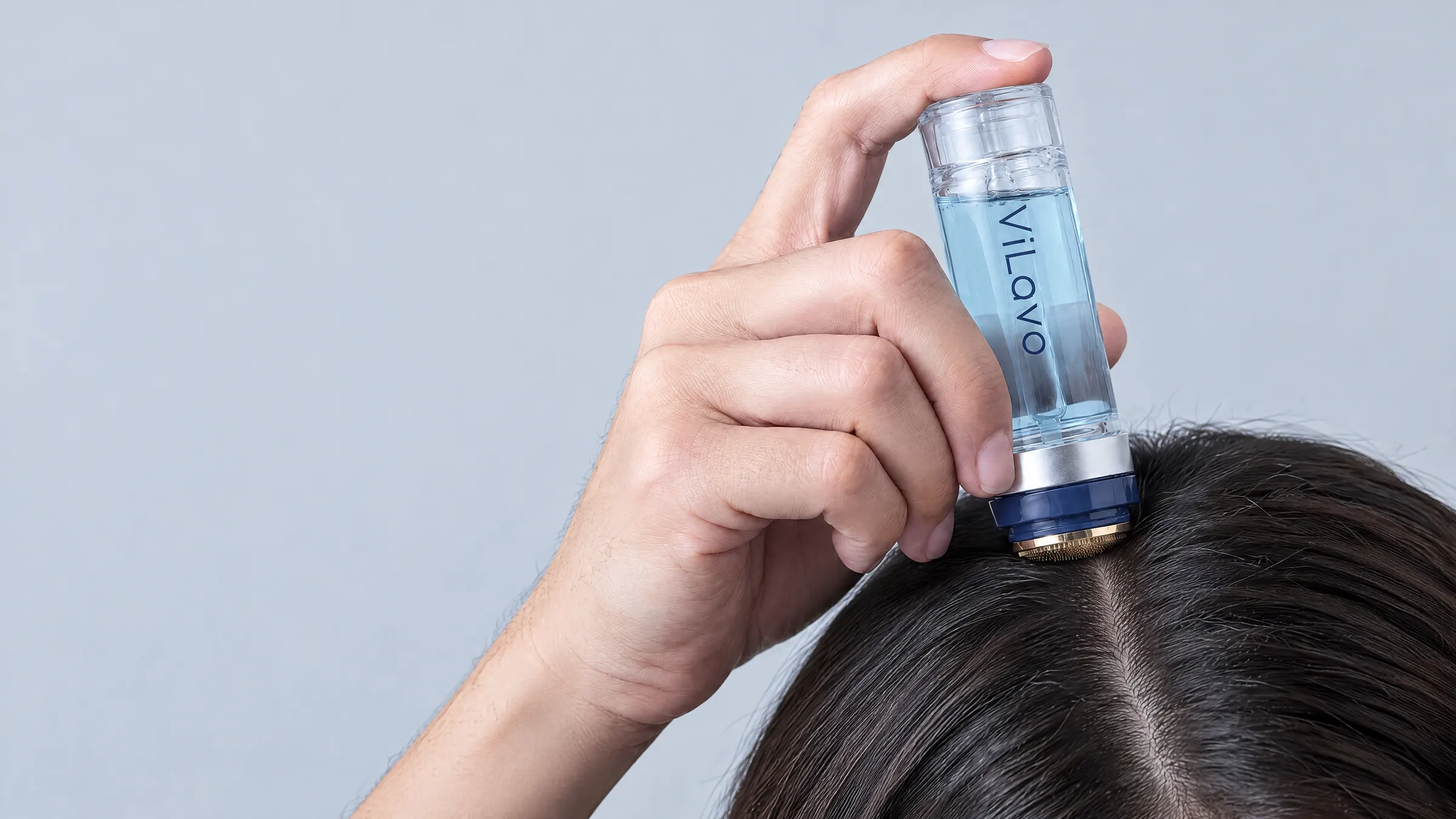 A hand pressing the ViLavo micro-infusion applicator against a natural part in dark hair